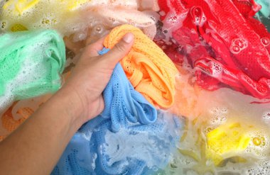 Beton zeminde toz deterjana batırılmış bir bebeğin renkli kıyafetlerini tutan kadın. Çamaşır konsepti kuru ve temiz.