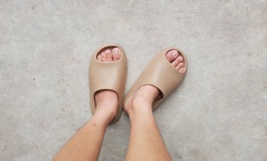 Çimento zemin zemininde açık ayak parmağı yastığı olan bir çift slayt içinde kadın bacakları. Kadın modası. Kadın yaz ayakkabıları, yumuşak terlikler.