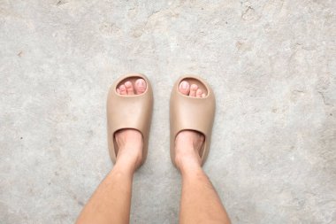 Çimento zemin zemininde açık ayak parmağı yastığı olan bir çift slayt içinde kadın bacakları. Kadın modası. Kadın yaz ayakkabıları, yumuşak terlikler.
