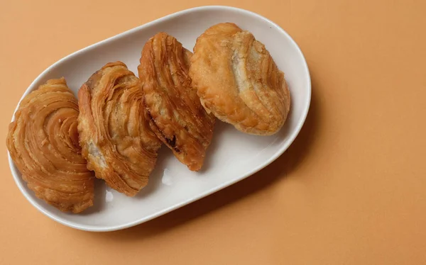 deep fried curry puff,curry puff pastry, karipap,epok epok, spiral curry puff isolated a orange pastel backdrop . thai curry puff concept.this pastry is asian traditional snacks
