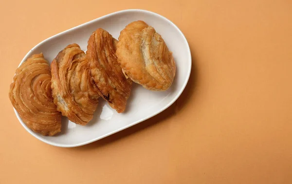 deep fried curry puff,curry puff pastry, karipap,epok epok, spiral curry puff isolated a orange pastel backdrop . thai curry puff concept.this pastry is asian traditional snacks