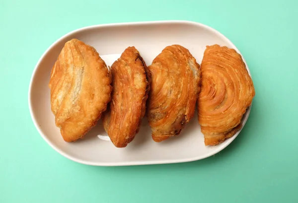 deep fried curry puff,curry puff pastry, karipap,epok epok, spiral curry puff isolated a green pastel backdrop . thai curry puff concept.this pastry is asian traditional snacks
