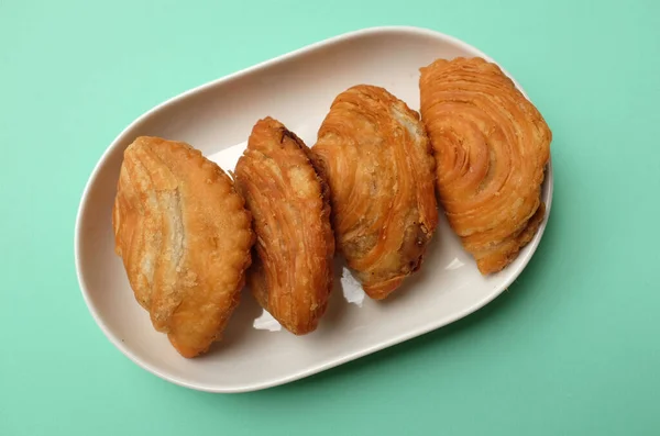 deep fried curry puff,curry puff pastry, karipap,epok epok, spiral curry puff isolated a green pastel backdrop . thai curry puff concept.this pastry is asian traditional snacks