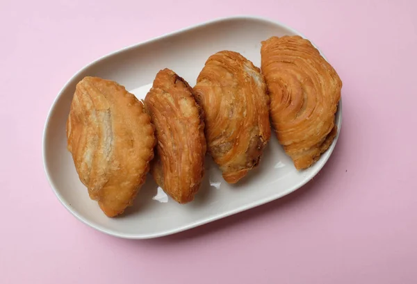deep fried curry puff,curry puff pastry, karipap,epok epok, spiral curry puff isolated a pink pastel backdrop . thai curry puff concept.this pastry is asian traditional snacks