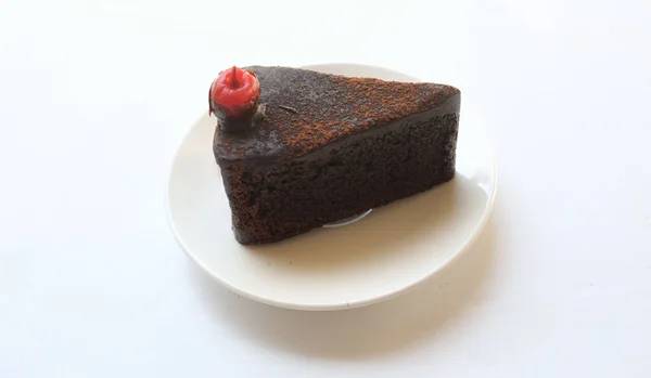 白い背景に隔離された赤いチェリーで飾られた層状のダークチョコレートケーキの一部を平らに見ます — ストック写真