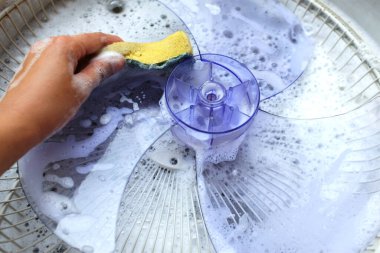 Asyalı genç bir kadın, suyu yıkamak için elektrikli vantilatör getirmek için toz dolu vantilatörü söker. Deterjanla ovala. ev işi temizlik konsepti