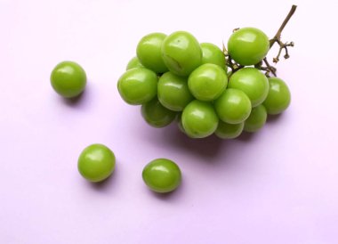 Bir demet taze yeşil parlak muscat (vitis vinifera) üzümü ve yaprağı güzel bir mor arka damlada izole edilmiş. Yeşil üzümler. Japon üzümleri.