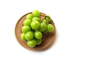 Beyaz arka planda izole edilmiş ahşap bir kapta taze tatlı yeşil muscat (Vitis vinifera) üzüm ve yaprak. Yeşil üzümler. Japon üzümleri