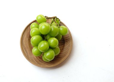 Beyaz arka planda izole edilmiş ahşap bir kapta taze tatlı yeşil muscat (Vitis vinifera) üzüm ve yaprak. Yeşil üzümler. Japon üzümleri