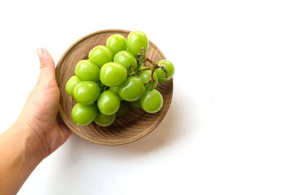 白い背景に隔離された木製皿に新鮮な甘い緑色の輝きのマスカット ビティスワニ の美しい束を握る手 緑のブドウ 日本のブドウ — ストック写真