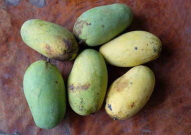 Bir yığın mango, koyu kahverengi ahşap masada yeşil yapraklı tropikal meyve. Üst görünüm ve düz uzanma.