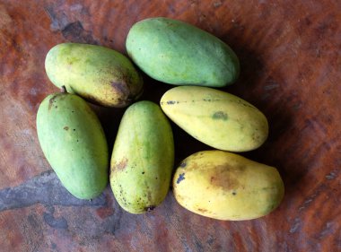 Bir yığın mango, koyu kahverengi ahşap masada yeşil yapraklı tropikal meyve. Üst görünüm ve düz uzanma.