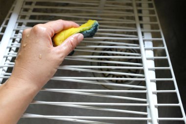Kadın elini sarı bir süngerle yıkar, buzdolabının raflarını temizler, buzdolabının yüzeyini mikrofiber bezle temizler, buzdolabını deterjanla yıkar. Temizlik servisi, ev hanımı., 