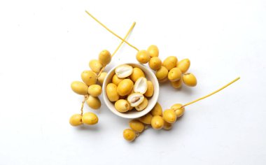 Beyaz arka planda izole edilmiş yeşil bir yaprağın üzerindeki bir kâse içinde bir avuç sarı hurma. Tayland meyvesi