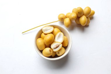 Beyaz arka planda izole edilmiş yeşil bir yaprağın üzerindeki bir kâse içinde bir avuç sarı hurma. Tayland meyvesi