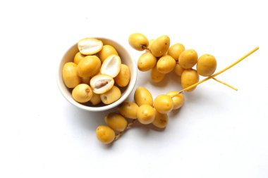 Beyaz arka planda izole edilmiş yeşil bir yaprağın üzerindeki bir kâse içinde bir avuç sarı hurma. Tayland meyvesi