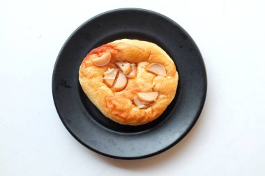 Üst ve düz daire şeklinde sosis, peynir, domates sosu, hamurdan yapılmış, beyaz bir zemin üzerinde pişirilerek olgunlaşan küçük bir pizza yatıyordu.