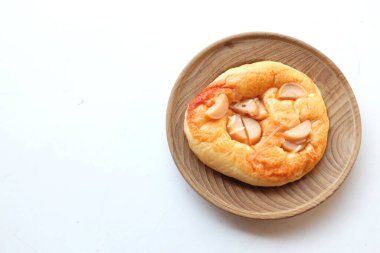 Üst ve düz daire şeklinde sosis, peynir, domates sosu, hamurdan yapılmış, beyaz bir zemin üzerinde pişirilerek olgunlaşan küçük bir pizza yatıyordu.