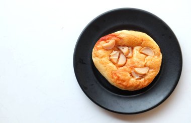 Üst ve düz daire şeklinde sosis, peynir, domates sosu, hamurdan yapılmış, beyaz bir zemin üzerinde pişirilerek olgunlaşan küçük bir pizza yatıyordu.