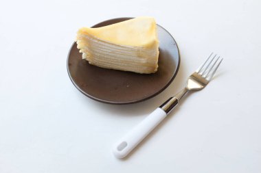 Üst ve düz bir porsiyon peynirli keki beyaz bir tabağa koyup tatlı olarak çatalla servis edip beyaz bir arkaplanda izole bir şekilde sergiliyor.