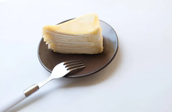 上の景色と平らなレイヤーチーズケーキの一部を白いプレートに置き 白い背景に単離されたデザートのフォークを提供します — ストック写真