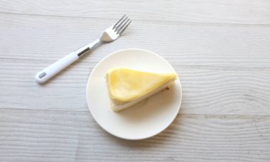 Üst ve düz bir porsiyon peynirli keki beyaz bir tabağa koyup tatlı olarak çatalla servis eder beyaz ahşap bir arka planda izole eder.