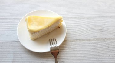 Üst ve düz bir porsiyon peynirli keki beyaz bir tabağa koyup tatlı olarak çatalla servis eder beyaz ahşap bir arka planda izole eder.