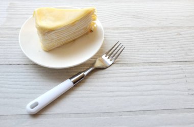 Üst ve düz bir porsiyon peynirli keki beyaz bir tabağa koyup tatlı olarak çatalla servis eder beyaz ahşap bir arka planda izole eder.