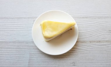 Üst ve düz bir porsiyon peynirli keki beyaz bir tabağa koyup tatlı olarak çatalla servis eder beyaz ahşap bir arka planda izole eder.