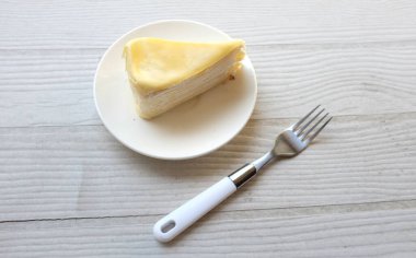 Üst ve düz bir porsiyon peynirli keki beyaz bir tabağa koyup tatlı olarak çatalla servis eder beyaz ahşap bir arka planda izole eder.