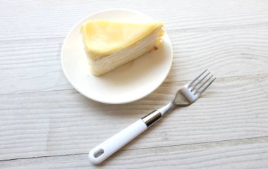 Üst ve düz bir porsiyon peynirli keki beyaz bir tabağa koyup tatlı olarak çatalla servis eder beyaz ahşap bir arka planda izole eder.