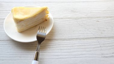 Üst ve düz bir porsiyon peynirli keki beyaz bir tabağa koyup tatlı olarak çatalla servis eder beyaz ahşap bir arka planda izole eder.