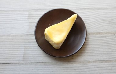 Üst ve düz bir porsiyon peynirli keki kahverengi bir tabağa koyuyor tatlı olarak çatalla servis ediliyor beyaz bir arkaplanda izole edilmiş.