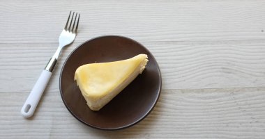 Üst ve düz bir porsiyon peynirli keki kahverengi bir tabağa koyuyor tatlı olarak çatalla servis ediliyor beyaz bir arkaplanda izole edilmiş.