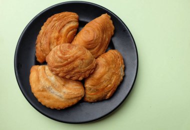 Körili poğaça resmi, yerel olarak Karipap olarak bilinen kıvırcık poğaça, yeşil bir pastel üzerinde izole edilmiş, çıtır çıtır kabuklu geleneksel çerez. Thai çıtır körili puf kavramı.