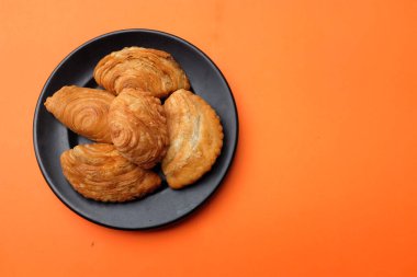 Körili poğaça resmi, yerel adıyla Karipap turuncu arka planda izole edilir. Çıtır kabuklu geleneksel çerez. Thai çıtır körili puf kavramı.