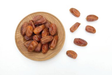 Lezzetli kuru hurma yığınları veya palmiye ağaçları veya ahşap bir tabakta Dactylifera meyvesi beyaz bir arka planda izole edilir. Atıştırmalık sağlıklı, Arap yemeği, tropikal meyve