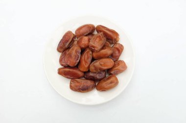 Lezzetli kuru hurma yığınları veya palmiye ağaçları veya beyaz bir tabakta bulunan palmiye anka kuşu dactylifera meyveleri beyaz bir arka planda izole edilir. Atıştırmalık sağlıklı, Arap yemeği, tropikal meyve