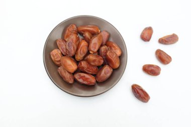 Lezzetli kuru hurma yığınları veya palmiye ağaçları veya kahverengi bir tabakta bulunan palmiye anka kuşu dactylifera meyveleri beyaz bir arka planda izole edilir. Atıştırmalık sağlıklı, Arap yemeği, tropikal meyve