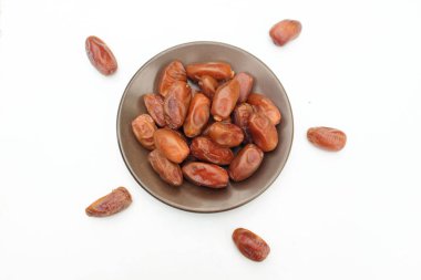 Lezzetli kuru hurma yığınları veya palmiye ağaçları veya kahverengi bir tabakta bulunan palmiye anka kuşu dactylifera meyveleri beyaz bir arka planda izole edilir. Atıştırmalık sağlıklı, Arap yemeği, tropikal meyve