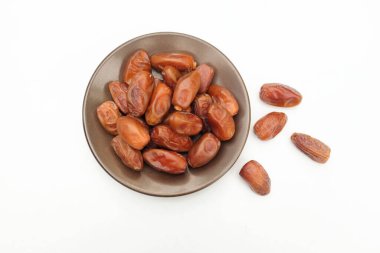 Lezzetli kuru hurma yığınları veya palmiye ağaçları veya kahverengi bir tabakta bulunan palmiye anka kuşu dactylifera meyveleri beyaz bir arka planda izole edilir. Atıştırmalık sağlıklı, Arap yemeği, tropikal meyve