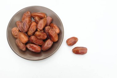 Lezzetli kuru hurma yığınları veya palmiye ağaçları veya kahverengi bir tabakta bulunan palmiye anka kuşu dactylifera meyveleri beyaz bir arka planda izole edilir. Atıştırmalık sağlıklı, Arap yemeği, tropikal meyve