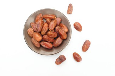 Lezzetli kuru hurma yığınları veya palmiye ağaçları veya kahverengi bir tabakta bulunan palmiye anka kuşu dactylifera meyveleri beyaz bir arka planda izole edilir. Atıştırmalık sağlıklı, Arap yemeği, tropikal meyve