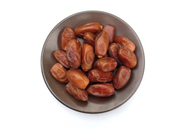 Lezzetli kuru hurma yığınları veya palmiye ağaçları veya kahverengi bir tabakta bulunan palmiye anka kuşu dactylifera meyveleri beyaz bir arka planda izole edilir. Atıştırmalık sağlıklı, Arap yemeği, tropikal meyve