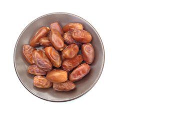 Lezzetli kuru hurma yığınları veya palmiye ağaçları veya kahverengi bir tabakta bulunan palmiye anka kuşu dactylifera meyveleri beyaz bir arka planda izole edilir. Atıştırmalık sağlıklı, Arap yemeği, tropikal meyve