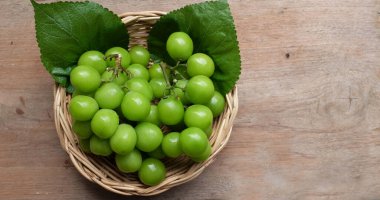 Bahçedeki ahşap masadaki bambu sepetinde taze tatlı yeşil Muscat (Vitis vinifera) üzüm ve yaprak. Japon üzümleri. Üzüm yeşili. Tadı tatlı ve doğal.