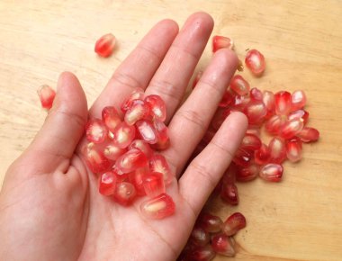 Asyalı bir kadının ellerinde taze olgun nar tohumları izole edilmiş eski ahşap arka planda. Kırmızı punica granatum sulu tahıllar en üstte.