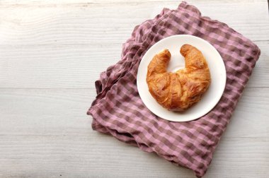 Yeni pişmiş kruvasanlardan oluşan lezzetli bir kahvaltı beyaz ahşap bir masada pembe bir kumaş üzerinde güzel bir tabakta servis edilir.