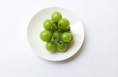 Beyaz arka planda izole edilmiş beyaz bir tabağa yerleştirilmiş güzel bir misket üzümü demeti.