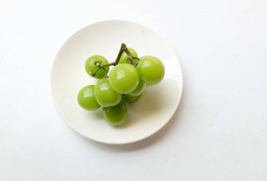 Beyaz arka planda izole edilmiş beyaz bir tabağa yerleştirilmiş güzel bir misket üzümü demeti.